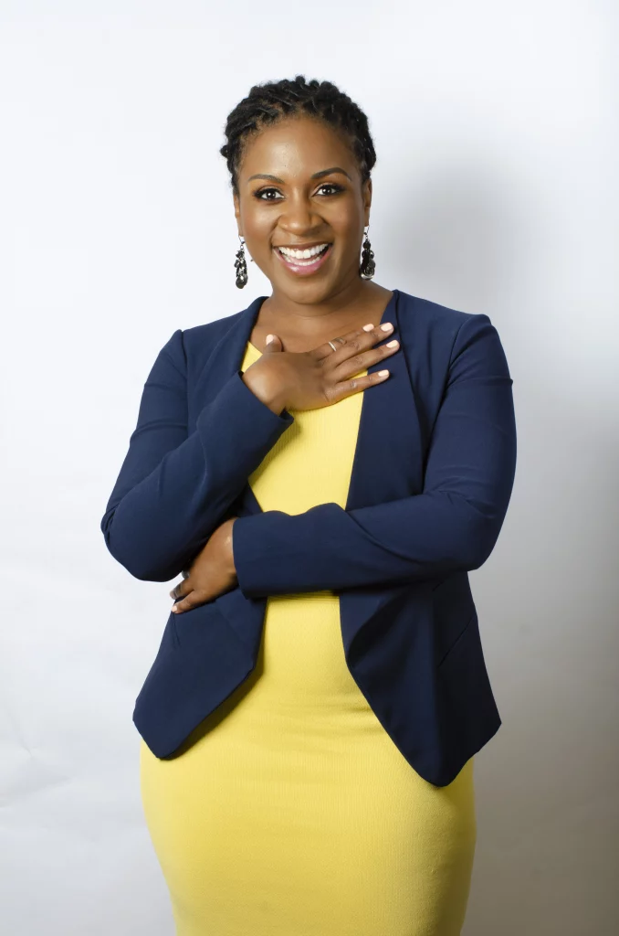 Jennifer Tardy posing in yellow drress with hand on chest
